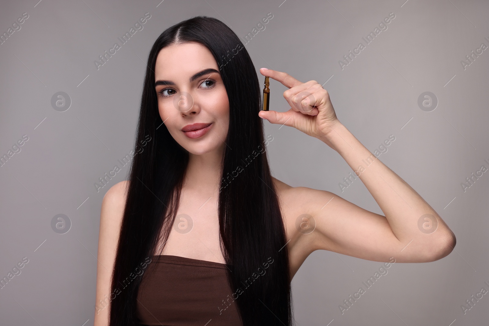 Photo of Beautiful young woman holding skincare ampoule on grey background