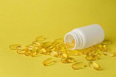 Photo of Open medicine bottle with scattered pills on yellow background, space for text