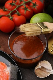 Tasty fish marinade, basting brush and products on wooden table, closeup