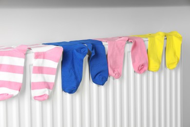 Different colorful socks on heating radiator near white wall