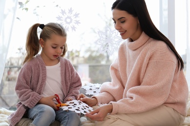 Mother and daughter making paper snowflake near window at home
