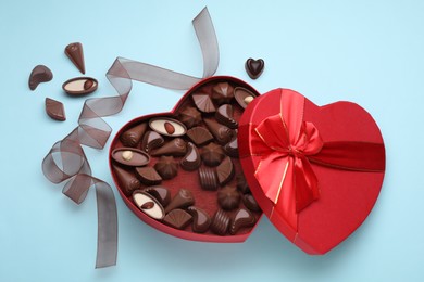 Heart shaped box with delicious chocolate candies and ribbon on light blue background, flat lay