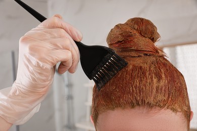 Young woman dyeing her hair with henna indoors, closeup