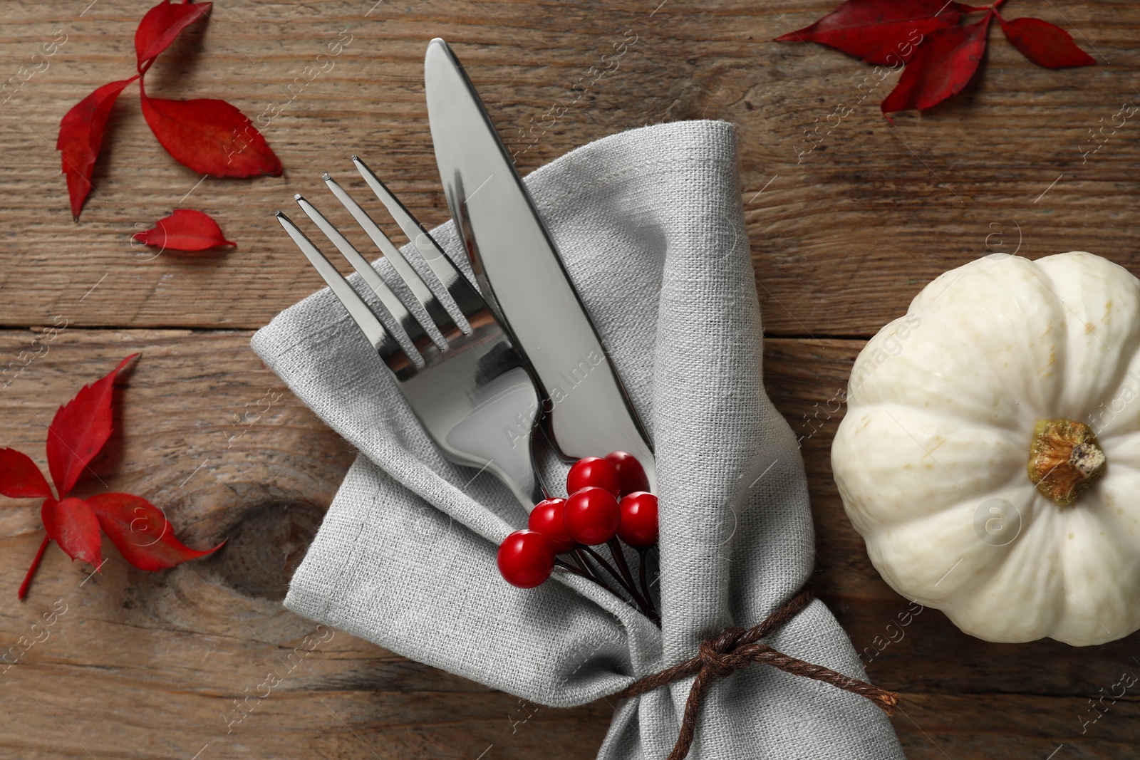 Photo of Thanksgiving table setting. Cutlery, napkin, autumn leaves and pumpkin on wooden background, flat lay