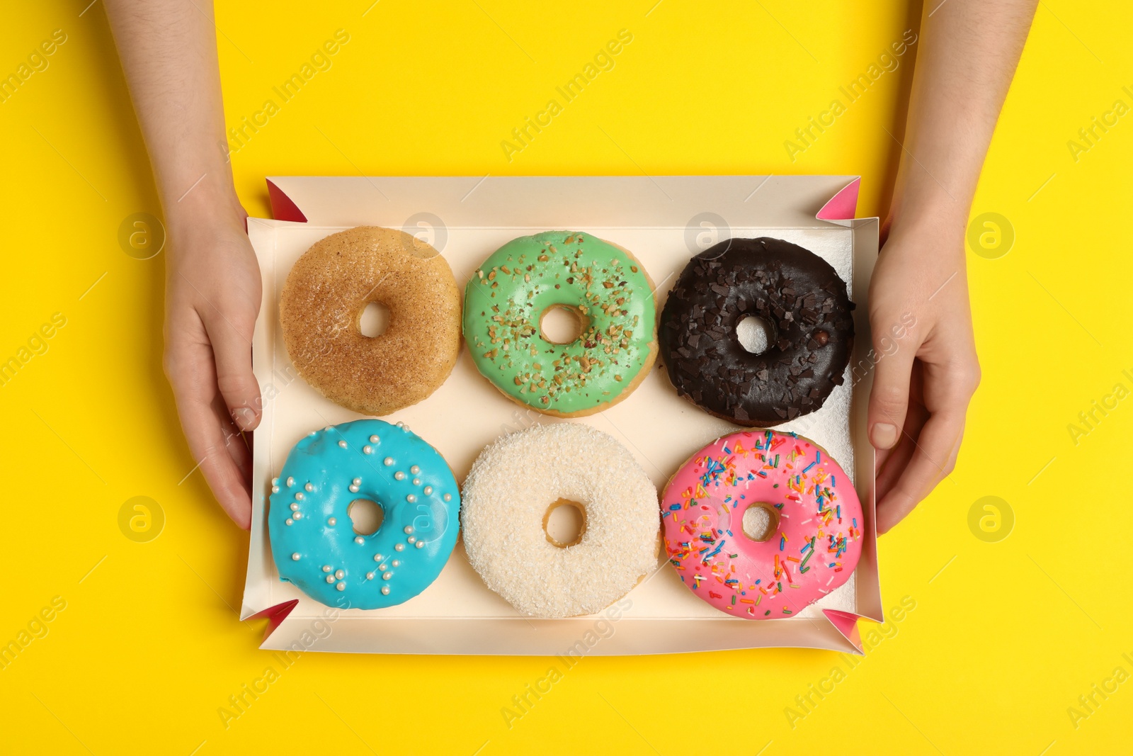 Photo of Woman with box of delicious donuts on yellow background, top view