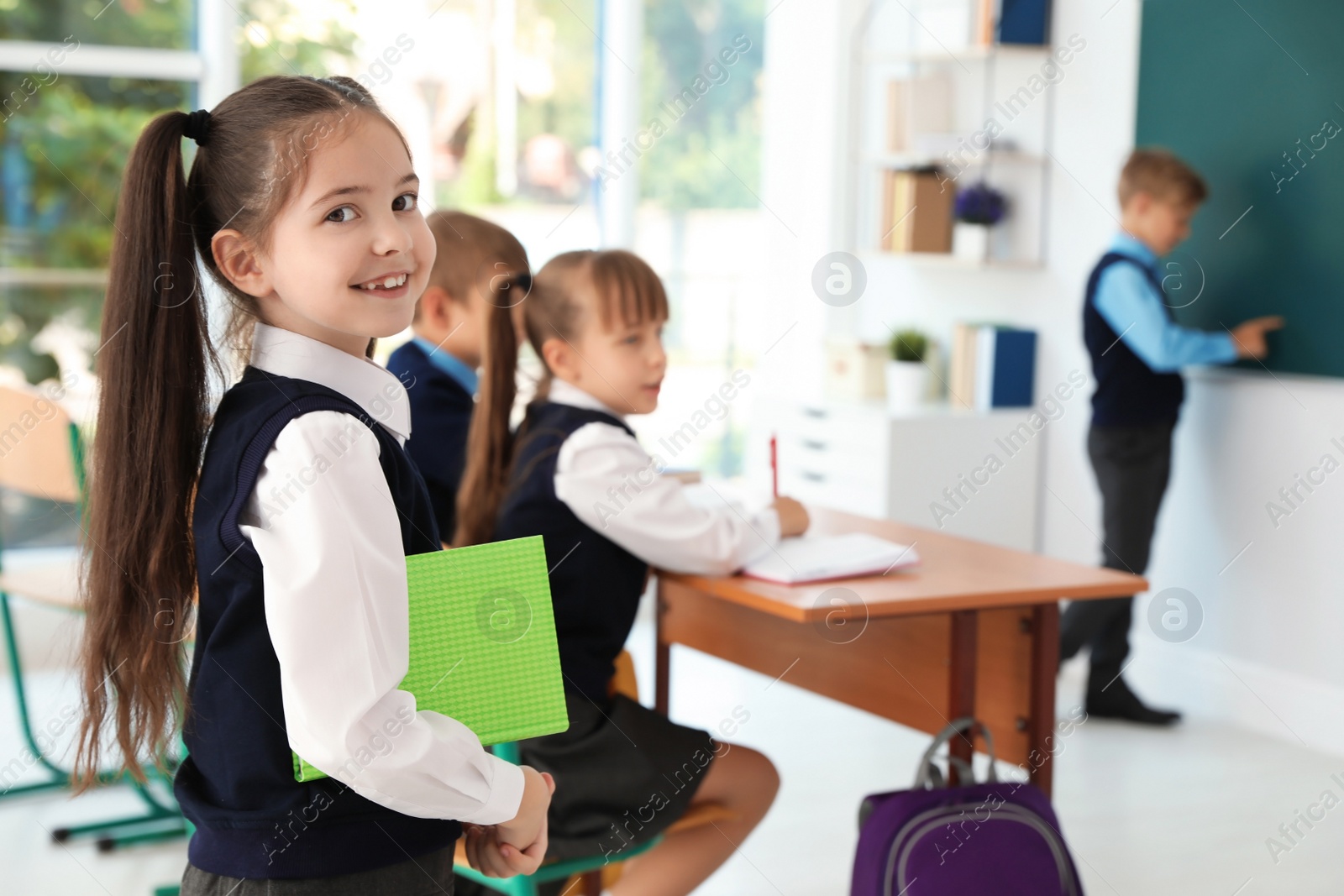 Photo of Little girl in classroom. Stylish school uniform