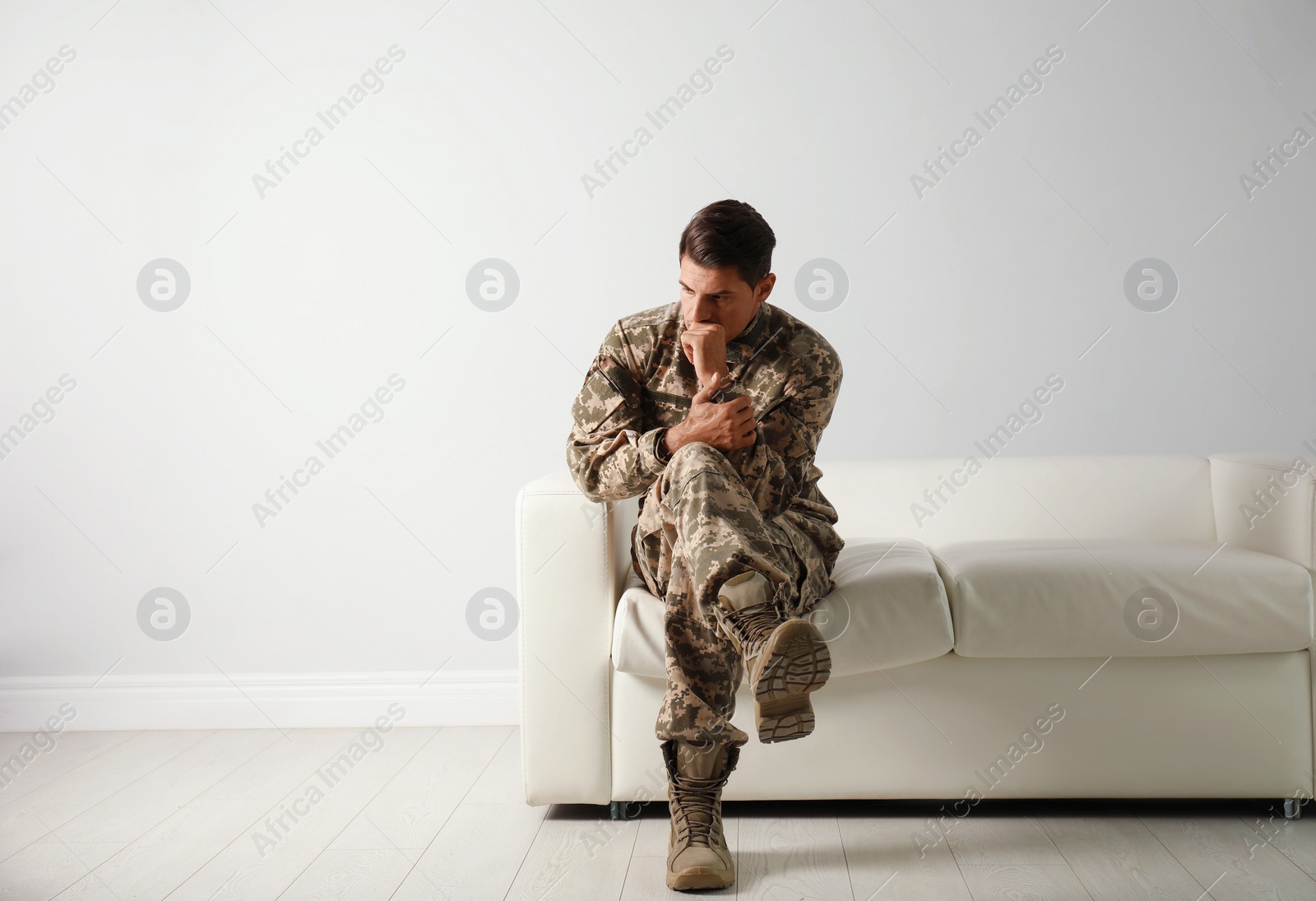 Photo of Stressed military officer sitting on sofa near white wall indoors. Space for text