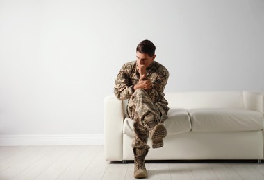 Photo of Stressed military officer sitting on sofa near white wall indoors. Space for text