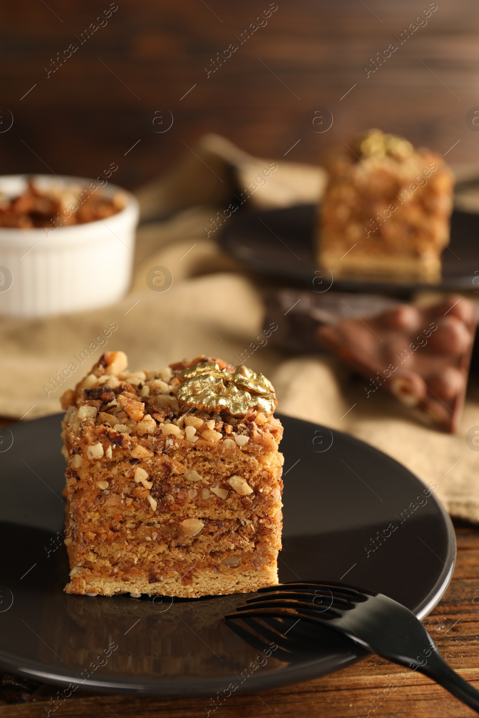 Photo of Piece of honey cake with walnuts and fork on plate, closeup