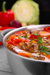 Photo of Saucepan of delicious vegetable soup with meat and ingredients on grey wooden table, closeup