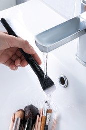 Photo of Woman washing makeup brush under stream of water in sink, closeup