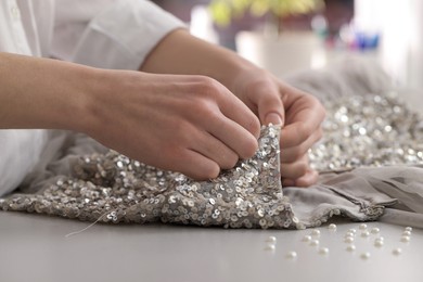Photo of Dressmaker sewing party dress from silver fabric with paillettes at table in atelier, closeup