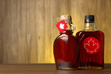 Photo of Glass bottles of tasty maple syrup on wooden table. Space for text