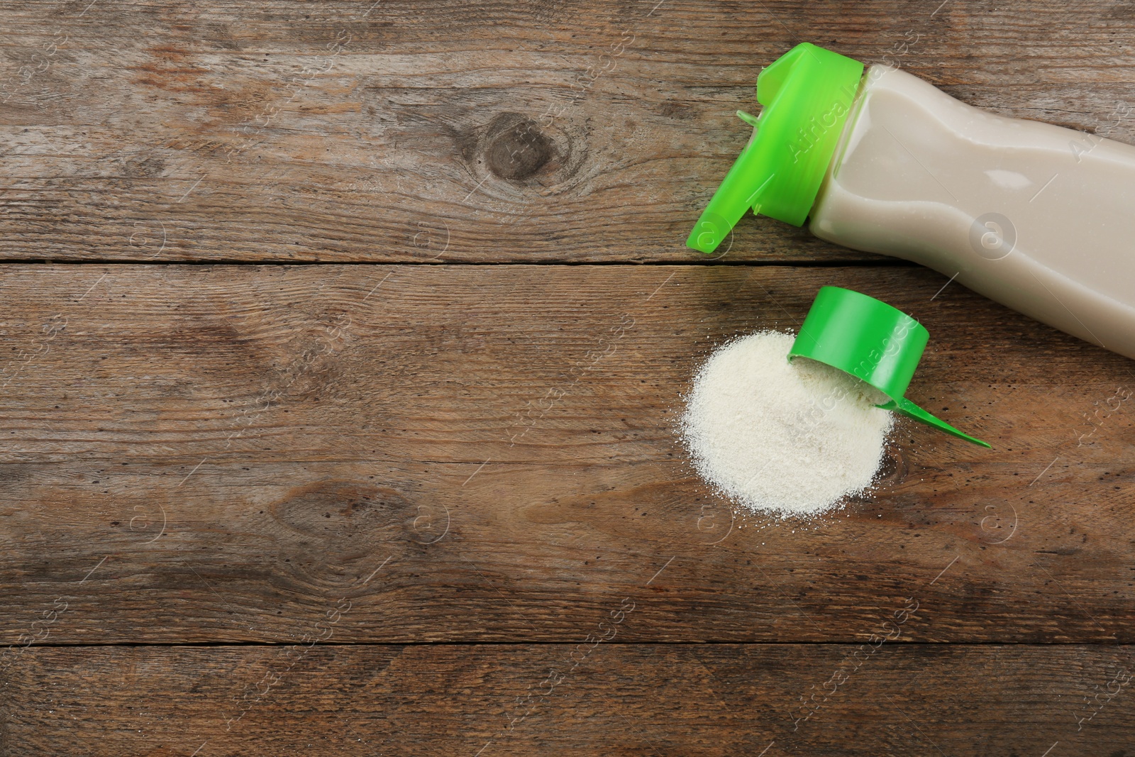 Photo of Measuring scoop of protein powder and bottle with shake on wooden table, flat lay. Space for text