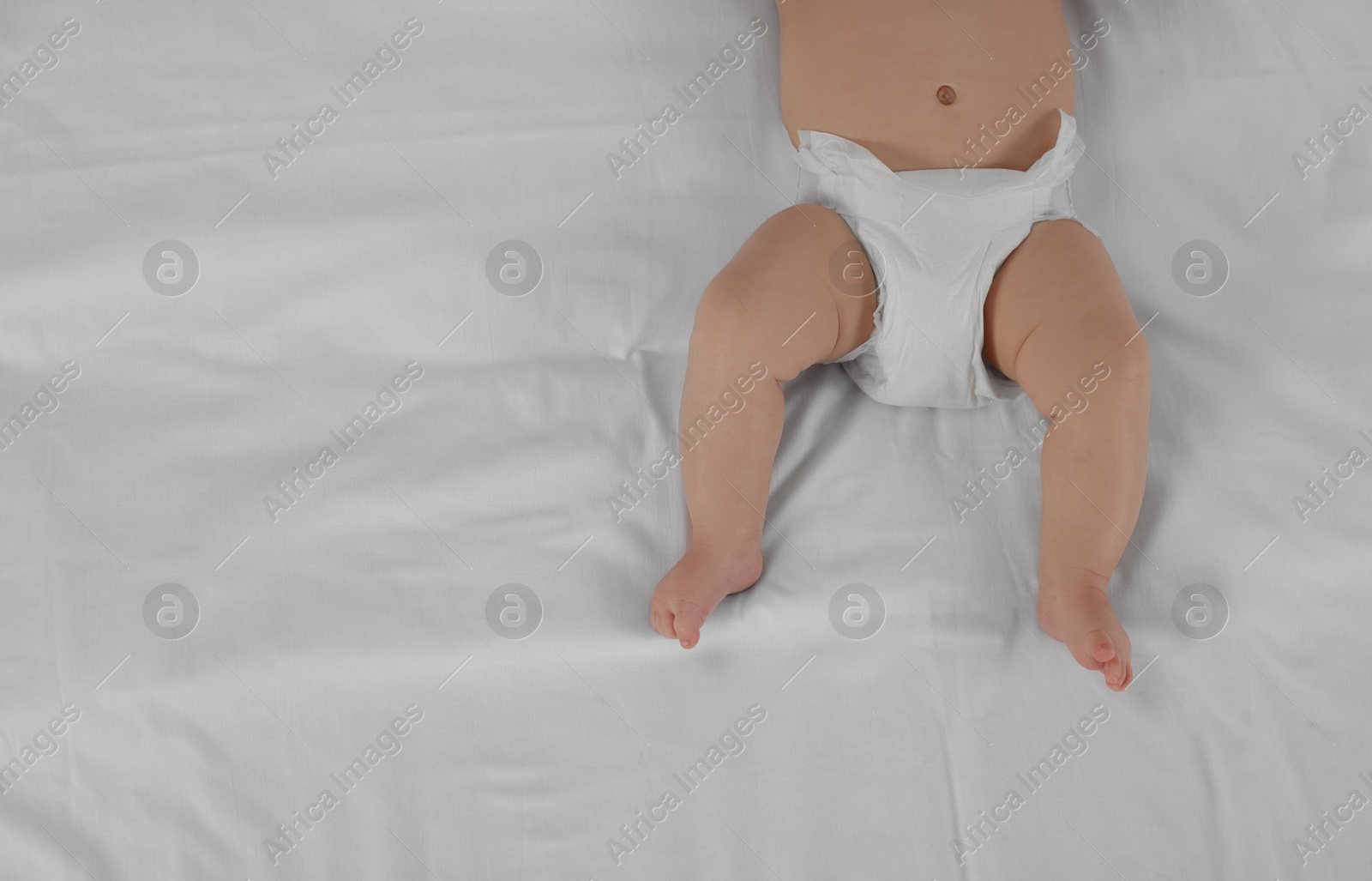 Photo of Little baby in diaper lying on bed, top view