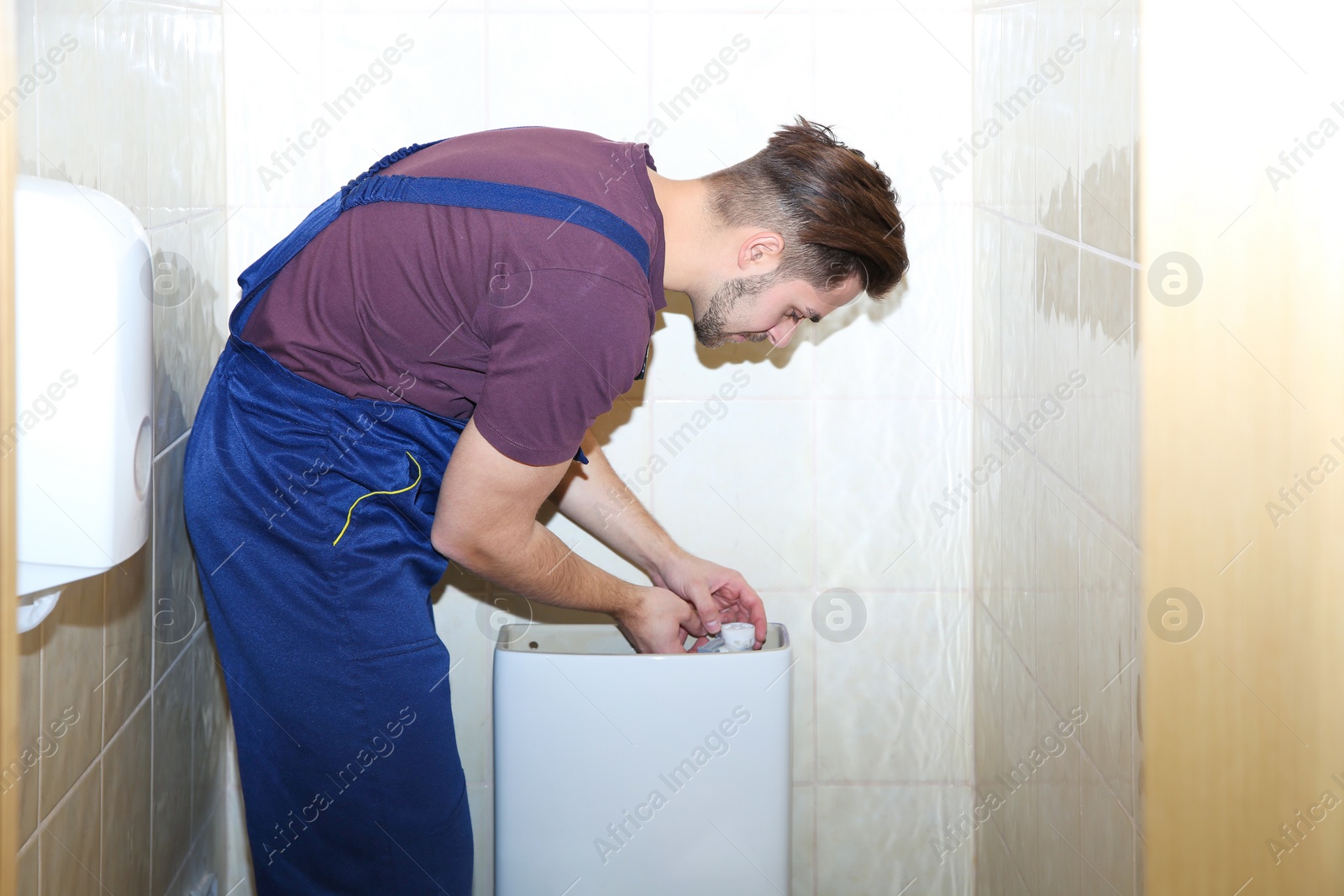 Photo of Male plumber repairing toilet tank in bathroom