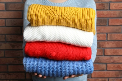 Photo of Woman holding pile of winter sweaters near brick wall, closeup view