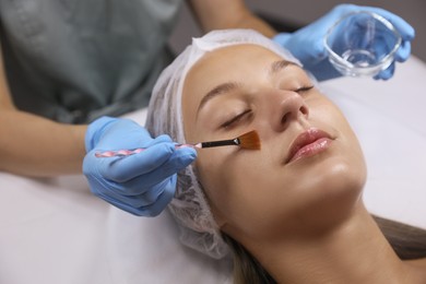 Photo of Cosmetologist applying chemical peel product on client's face in salon