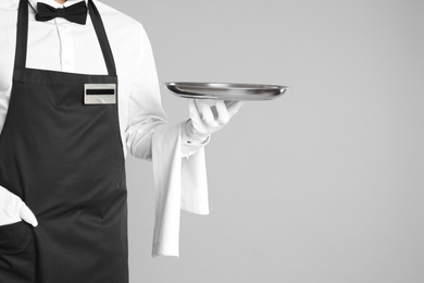 Photo of Waiter holding tray on light grey background, closeup. Space for text