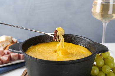 Photo of Dipping piece of bread into fondue pot with tasty melted cheese at table against gray background, closeup
