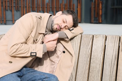 Tired man sleeping on bench outdoors. Space for text