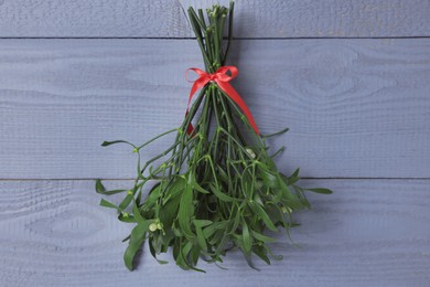 Photo of Mistletoe bunch with red bow hanging on grey wooden wall. Traditional Christmas decor