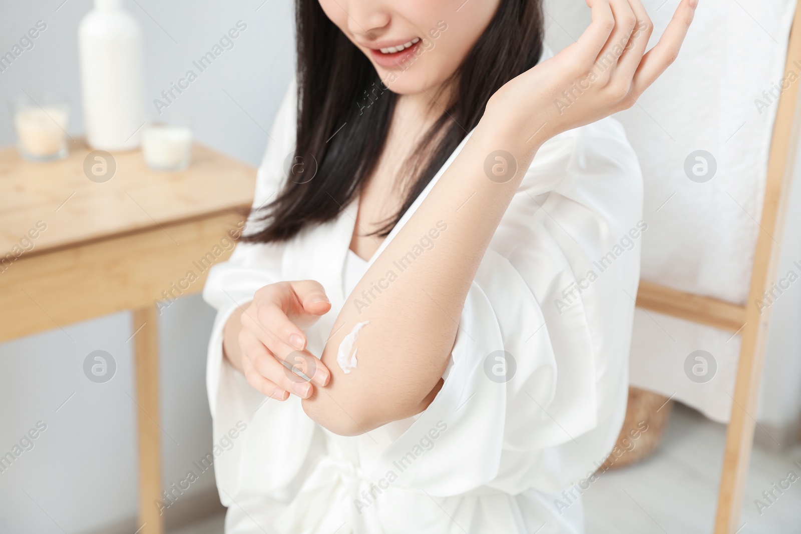 Photo of Young woman applying body cream on elbow in bathroom, closeup