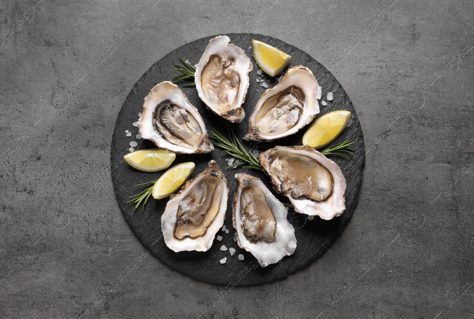 Photo of Delicious fresh oysters with lemon slices served on grey table, top view