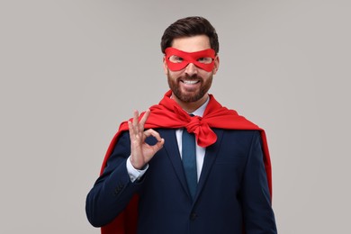 Photo of Happy businessman in red superhero cape and mask showing ok gesture on beige background