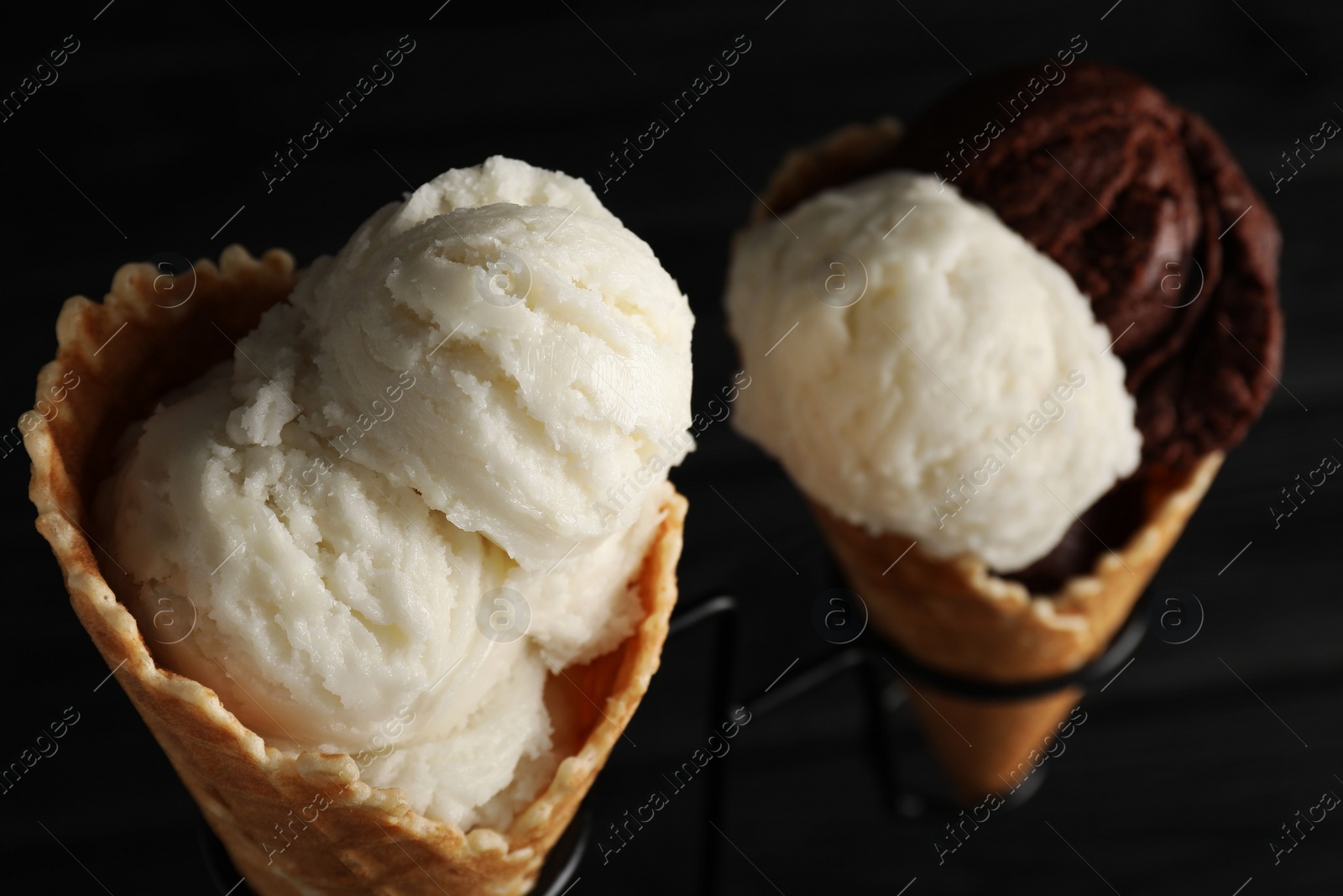 Photo of Ice cream scoops in wafer cones on stand against dark background, closeup