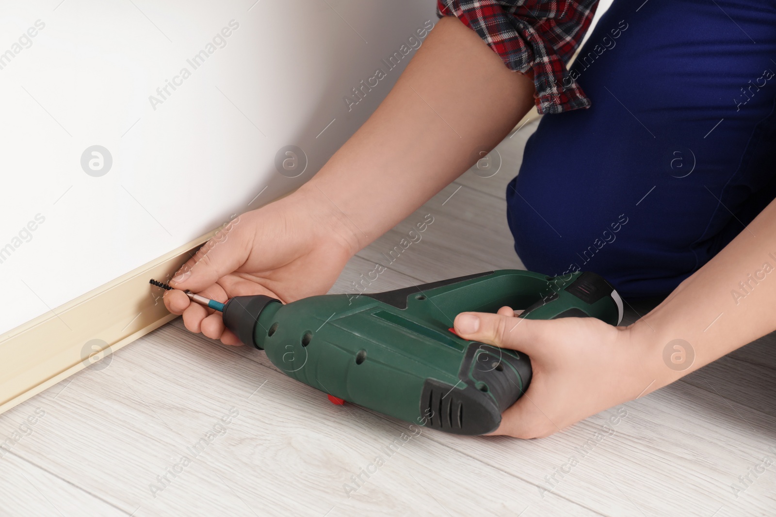Photo of Man installing plinth on laminated floor with screwdriver in room, closeup