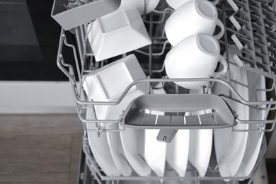 Open modern dishwasher with clean tableware, closeup