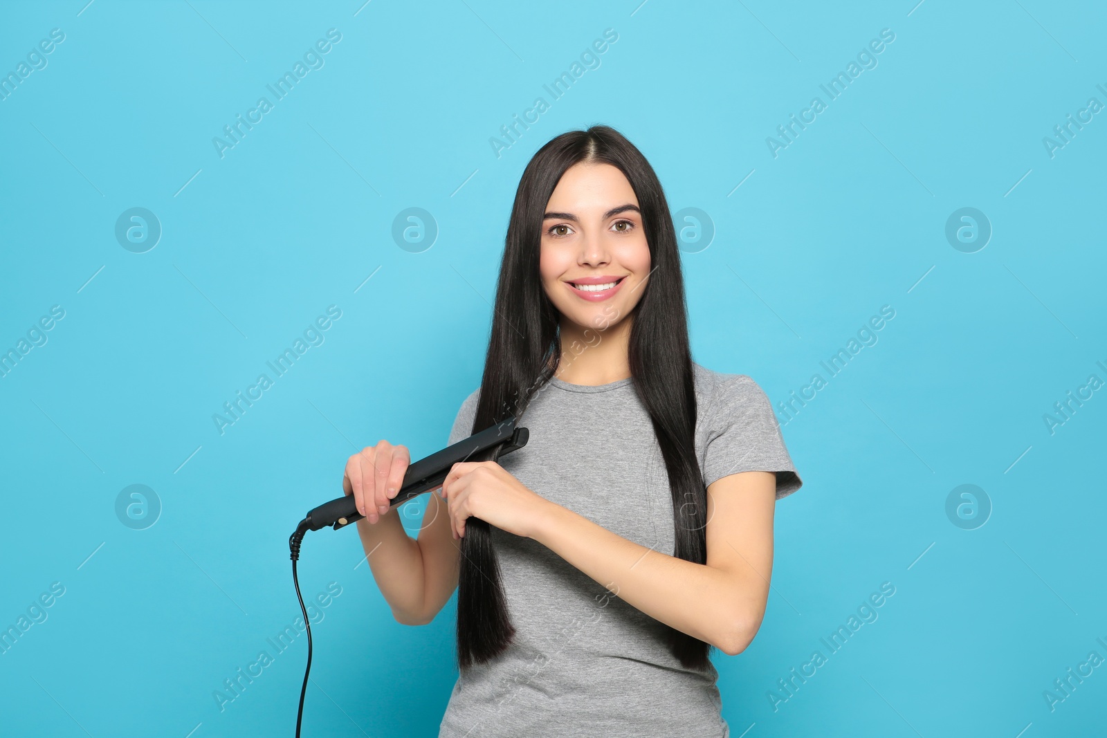 Photo of Beautiful happy woman using hair iron on light blue background