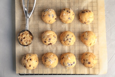 Photo of Raw cookie dough with chocolate chips and scoop on parchment paper, top view