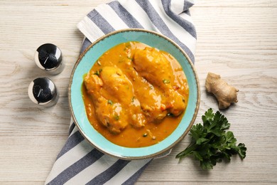 Tasty chicken curry, parsley and ginger on wooden table, flat lay