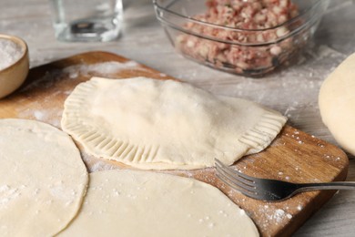 Raw chebureki with tasty filling and fork on wooden table, closeup