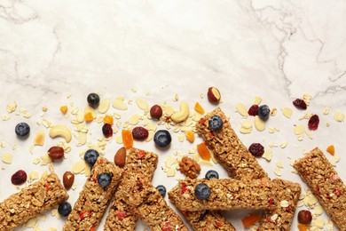 Photo of Tasty granola bars and ingredients on white marble table, flat lay. Space for text