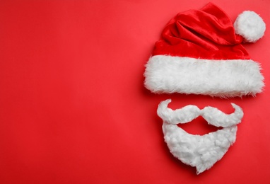 Photo of Santa Claus hat with white beard on red background, flat lay. Space for text