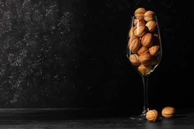 Photo of Tasty walnut shaped cookies served in glass for welcoming guests on black table against dark background, space for text