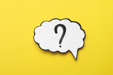 Paper speech bubble with question mark on yellow background, top view