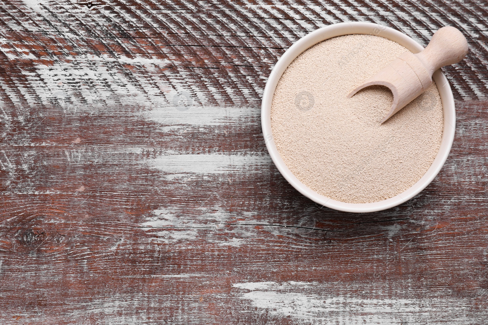 Photo of Bowl and scoop with active dry yeast on wooden table, top view. Space for text