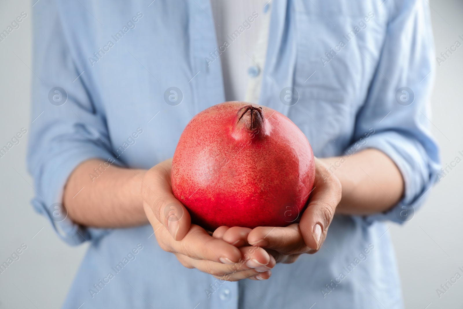 Photo of Woman holding ripe pomegranate on light background, closeup