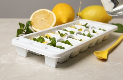 Photo of Pouring water into ice cube tray with mint and lemon on grey table