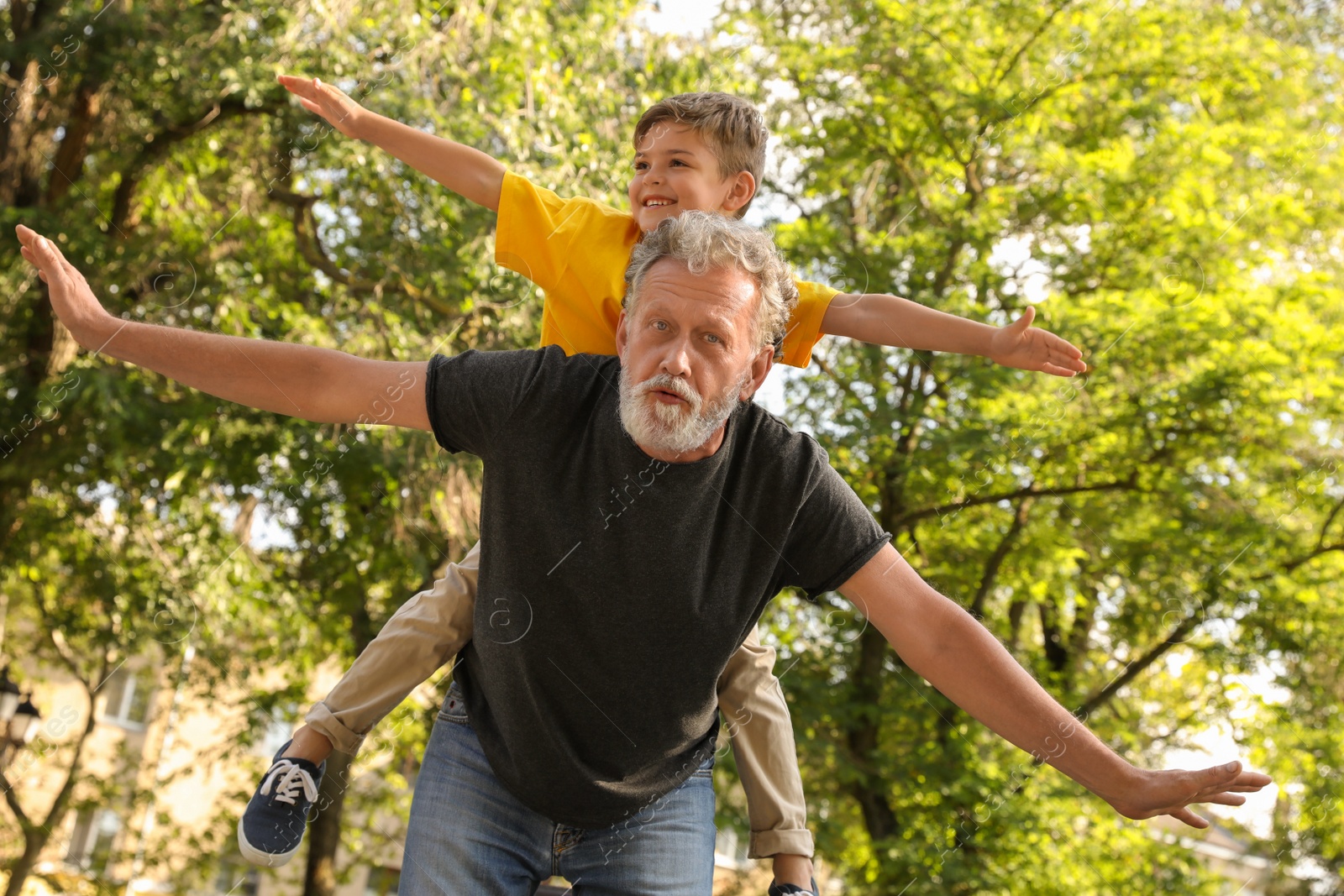 Photo of Senior man with his little grandson having fun together in park