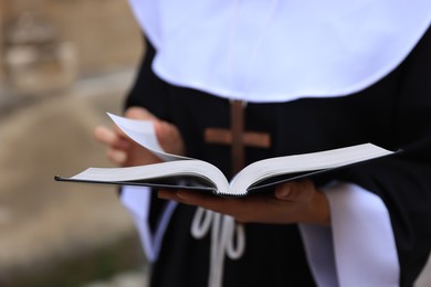 Photo of Young nun with Christian cross and Bible outdoors, closeup