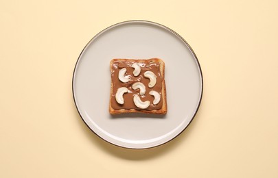 Photo of Toast with tasty nut butter and cashews on beige background, top view
