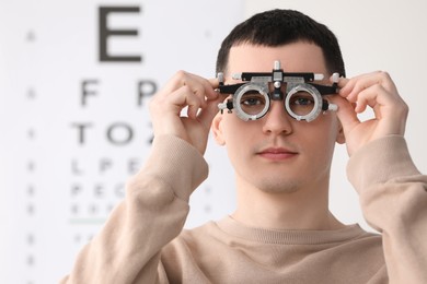 Photo of Young man with trial frame against vision test chart