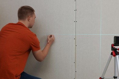 Photo of Man using cross line laser level and pencil for accurate measurement on plasterboard, back view