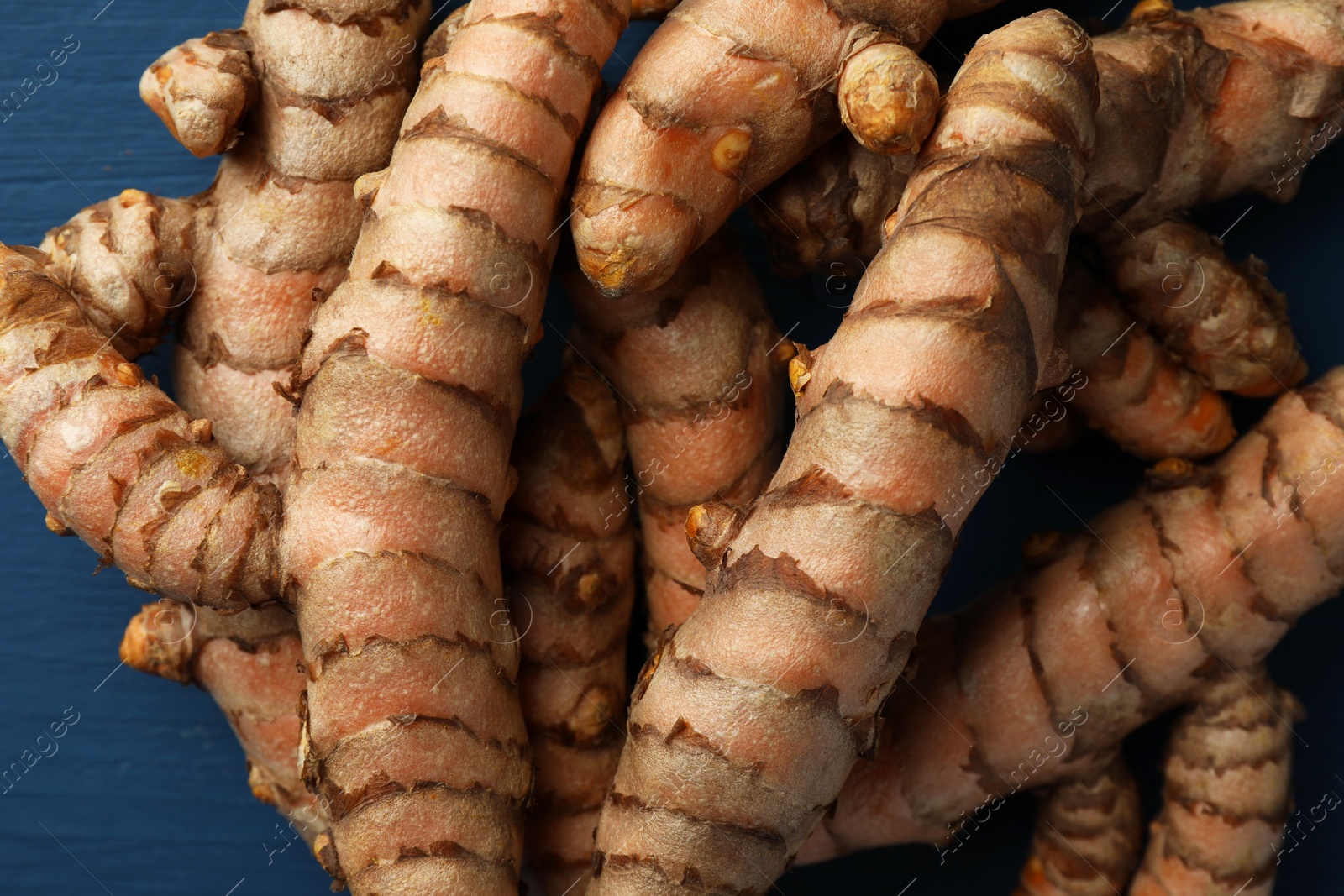 Photo of Many raw turmeric roots on blue table, flat lay
