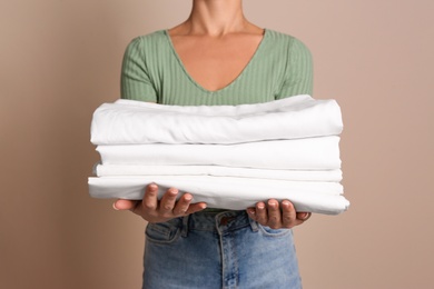 Photo of Woman holding stack of clean bed linens on beige background